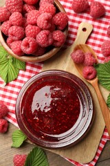 Tasty jam, fresh ripe raspberries and leaves on wooden table, flat lay