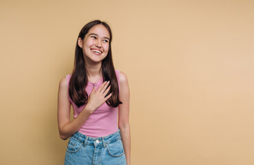 Smiling young woman poses with her hand on her chest against a warm yellow background during a...