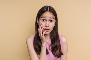 Young woman expresses surprise while touching her face against a light background