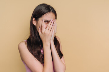 Young woman covers face with hands in expressive gesture against neutral background