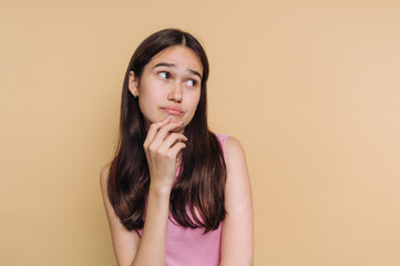 Young woman contemplating with thoughtful expression against a light background in a casual setting...
