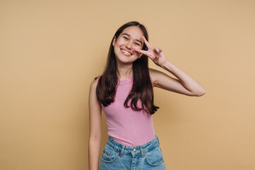 Fototapeta premium Young girl smiling and posing playfully against a yellow background in a casual outfit during a bright afternoon