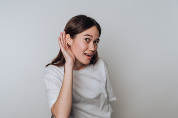 Young woman playfully listening with her hand to her ear against a neutral background