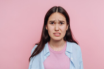 Fototapeta premium Young woman expressing discomfort against a pink background while wearing a casual outfit in a studio setting