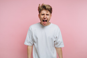 Man expressing strong emotions with a frustrated shout against a pastel pink backdrop during a...