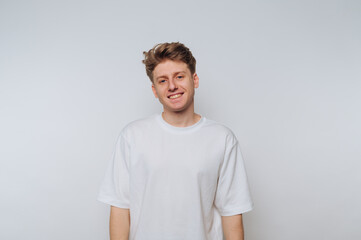 Young man smiles against a plain white background while dressed in a casual white t-shirt