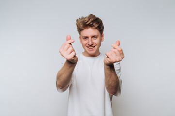 Young man making heart gestures with hands against a plain background in a casual setting