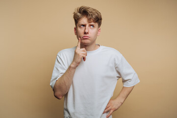 Young man in a white shirt pondering thoughtfully against a beige background with an expressive look