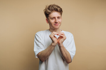 Young man making heart shape with hands against a neutral background, conveying affection and...