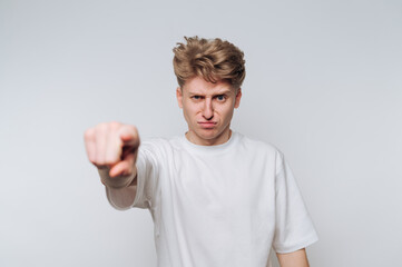 Young man expressing frustration while pointing directly at the camera in a neutral setting with...