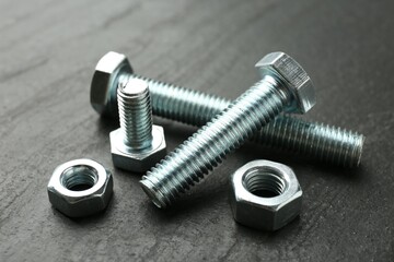 Metal bolts and nuts on black table, closeup