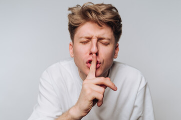Young man gestures for silence while wearing a white shirt against a neutral background during a...