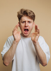 Young man expressing strong emotions with hands raised against a neutral background
