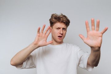 Young man expressing surprise with hands raised in a neutral backdrop during an indoor shoot