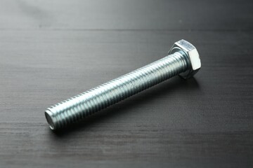 One metal bolt on dark wooden table, closeup