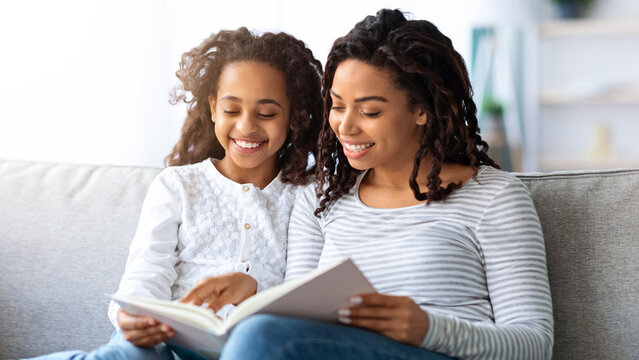 Family lifestyle, leisure activity concept. Happy black mother and daughter reading book together at home, copy space. Beautiful african american family mom and child reading fairy tales