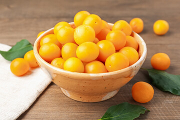 Ripe yellow cherry plums and leaves on wooden table, closeup
