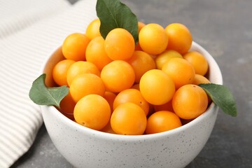Ripe yellow cherry plums and leaves on grey table, closeup