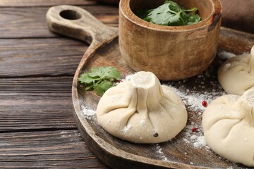 Uncooked khinkalis (dumplings) with peppercorns and parsley on wooden table, closeup