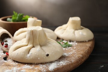Uncooked khinkalis (dumplings) with spices on wooden table, closeup