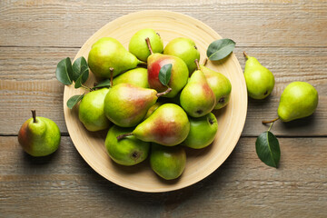 Fresh ripe pears and green leaves on wooden table, flat lay