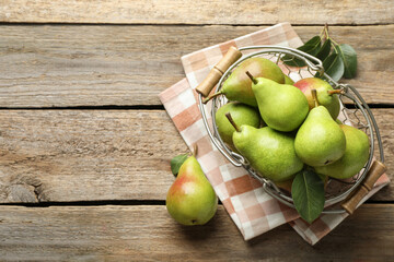 Fresh ripe pears in metal basket and green leaves on wooden table, flat lay. Space for text