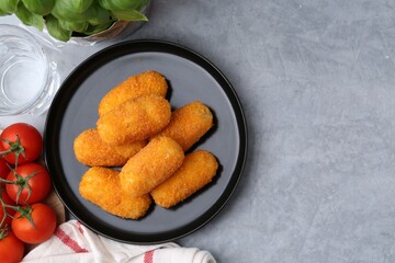 Delicious fried croquettes, glass of water, tomatoes and basil on gray textured table, flat lay. Space for text