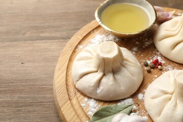 Uncooked khinkalis (dumplings) with peppercorns, flour and bay leaves on wooden table, closeup....