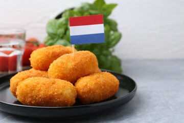 Delicious fried croquettes and flag of Netherlands on gray table, closeup
