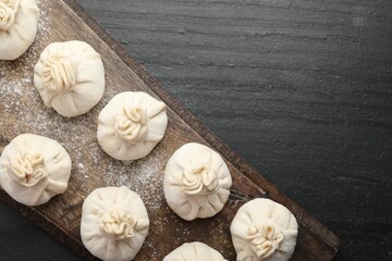 Uncooked khinkalis (dumplings) with flour on black table, top view. Space for text