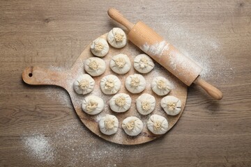 Uncooked khinkalis (dumplings) and rolling pin on wooden table, top view