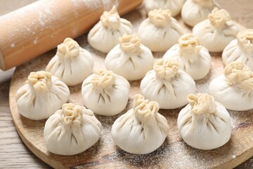 Uncooked khinkalis (dumplings) and rolling pin on wooden table, closeup