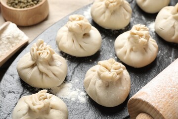 Uncooked khinkalis (dumplings), flour, spices and rolling pin on table, closeup