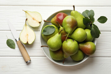 Fresh ripe pears, knife and green leaves on white wooden table, flat lay