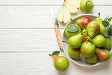 Fresh ripe pears, knife and green leaves on white wooden table, flat lay. Space for text