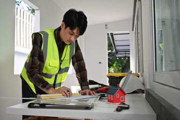 A Focused male engineer in a safety vest working on architectural plans at a construction site