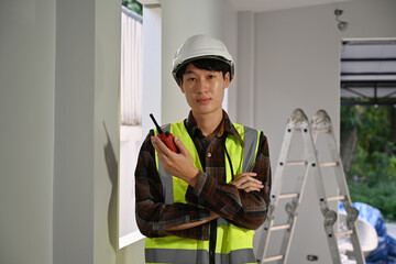 Portrait of an Asian male supervisor in hard hat and safety vest standing at an indoor job site...