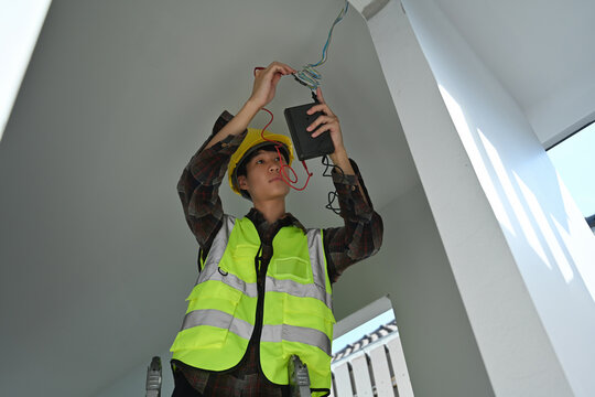 Male electrician in safety gear using a multimeter to check ceiling wiring during home construction