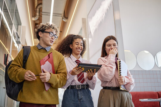 Group of multiethnic people walking in hallway, smiling and interacting while holding digital tablet and notebooks, showing cheerful expressions and casual body language