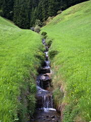 Scenic alpine landscape in South Tyrol with a waterfall, meadow, and forest.