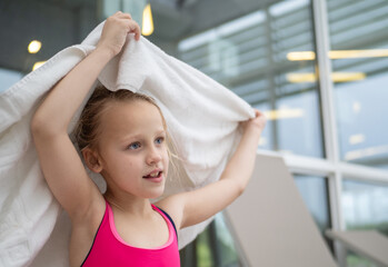 Little girl happily drying her hair with a towel after enjoying a refreshing swim in an indoor...