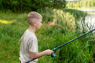 Teen boy casting fishing rod on a sunny summer day by the river or lake