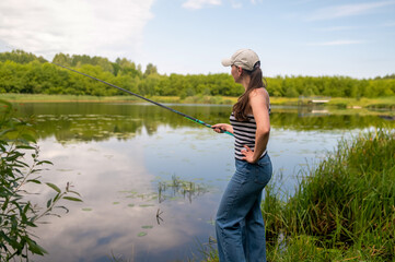 Young woman fishing with a rod standing on the lake shore on a calm summer day