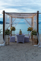 Wedding arch on coast. Romantic beach wedding setup featuring beautifully decorated arch with flowers and lights, elegant table for two and serene ocean view, creating dreamy atmosphere for couples