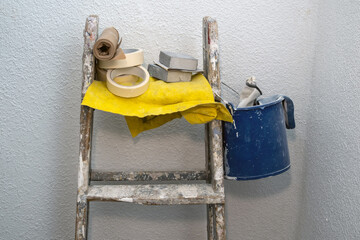 Renovation supplies arranged on wooden ladder, paint tools, masking tape, sandpaper, color palette,...