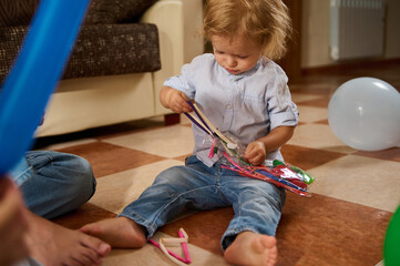 A young child enjoys playing on the floor with colorful toys and balloons indoors. The setting...