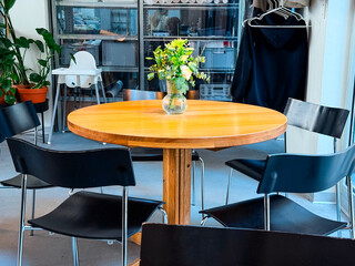 Round wooden table with vase of flowers inside cafe. Interior design, lifestyle, and social gathering.