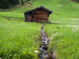 Traditional wooden hut with alpine meadow and stream in South Tyrol, Italy.