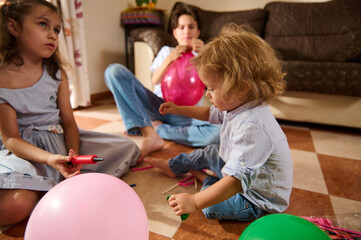 A group of kids gather in a cozy living room to inflate colorful balloons, sharing laughter and...