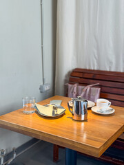 Wooden cafe table with coffee cup and metal teapot indoors. Dining lifestyle, casual atmosphere, and social comfort.